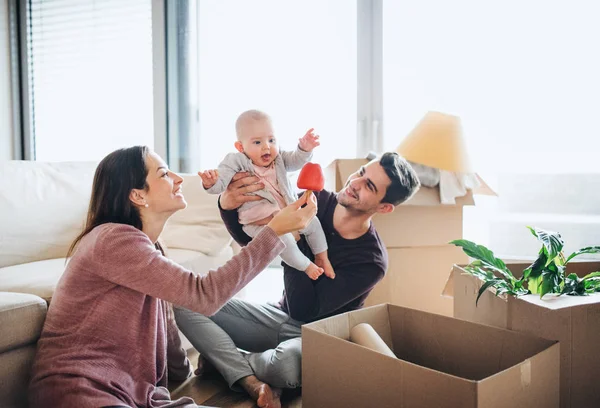 Un retrato de pareja joven con un bebé y cajas de cartón moviéndose en un nuevo hogar . — Foto de Stock