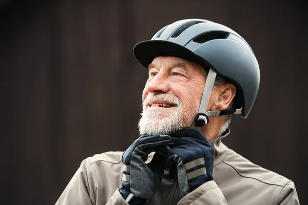 Ein aktiver Senior, der draußen in der Stadt steht und einen Fahrradhelm aufsetzt. — Stockfoto
