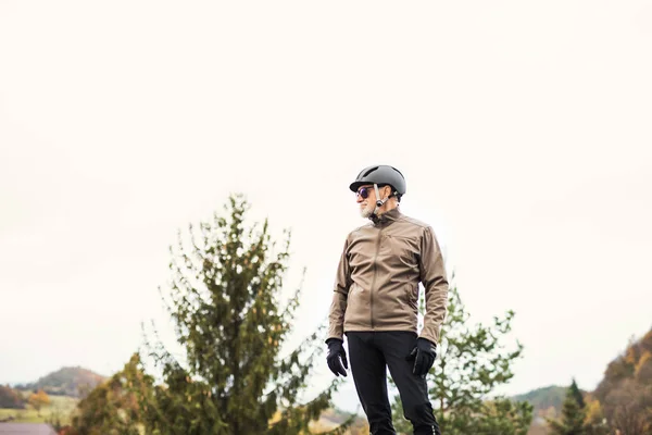 Ett porträtt av aktiv senior man med cykel hjälm stå utomhus i naturen. — Stockfoto