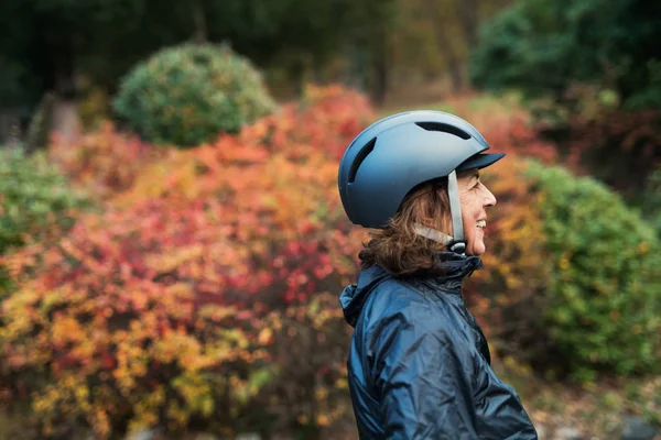 Στην πλαϊνή όψη ενεργό ανώτερος γυναίκα με ποδηλάτων κράνος στέκεται σε εξωτερικούς χώρους στη φύση. — Φωτογραφία Αρχείου