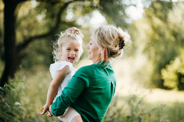 Joven madre en la naturaleza con una pequeña hija en brazos, divirtiéndose. Copiar espacio . — Foto de Stock