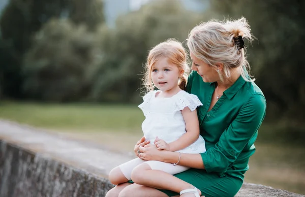 Jonge moeder in de natuur met kleine dochter, zittend op een stenen muur. — Stockfoto