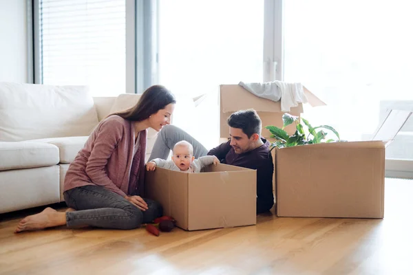 Un retrato de pareja joven con un bebé y cajas de cartón moviéndose en un nuevo hogar . —  Fotos de Stock