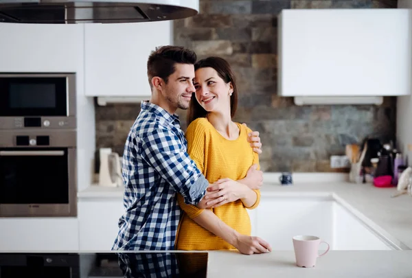 Una joven pareja enamorada de pie en una cocina en casa, abrazándose . — Foto de Stock