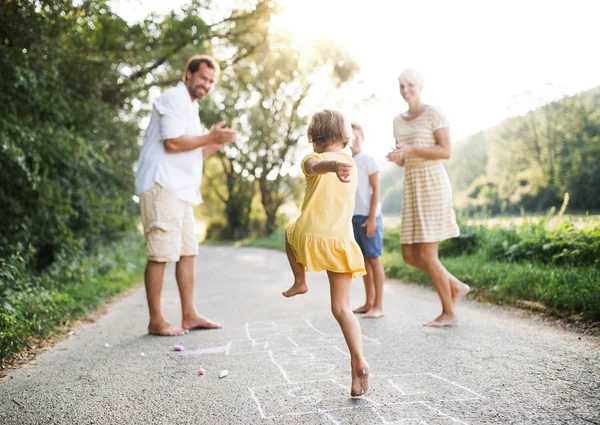Una giovane famiglia con bambini piccoli che giocano a hopscotch su una strada in estate . — Foto Stock
