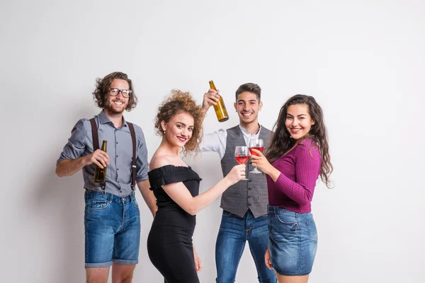 Portrait of young group of friends standing in a studio, holding bottles and glasses. — Stock Photo, Image