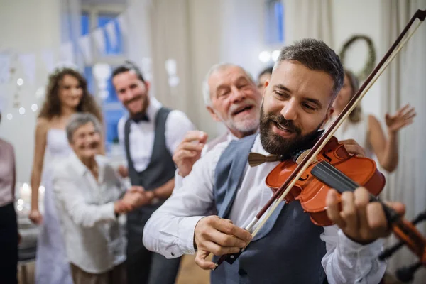 Un homme mûr jouant du violon lors d'une réception de mariage, mariée et marié dansant . — Photo