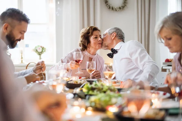 Um casal sênior sentado em uma mesa em uma festa de aniversário indoor, beijando . — Fotografia de Stock