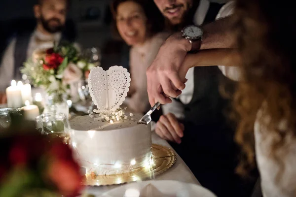 Um midsection do par jovem que se senta em uma mesa em um casamento, cortando um bolo . — Fotografia de Stock