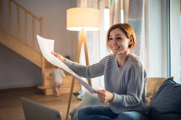 Ung kvinna med laptop och ritningar sitter inomhus, arbetar hemma. — Stockfoto