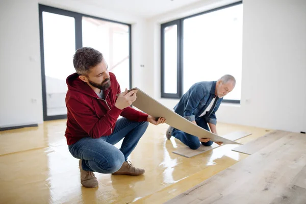 Un hombre maduro con su padre mayor colocando pisos de vinilo, un nuevo concepto de hogar . — Foto de Stock