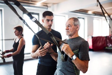 Bir grup genç bir kişisel antrenör Trx ile egzersiz yaparak ile spor salonunda neşeli yaşlılar.
