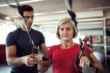 Trx ile egzersiz yaparak genç bir eğitmen ile spor salonunda kadın kıdemli.