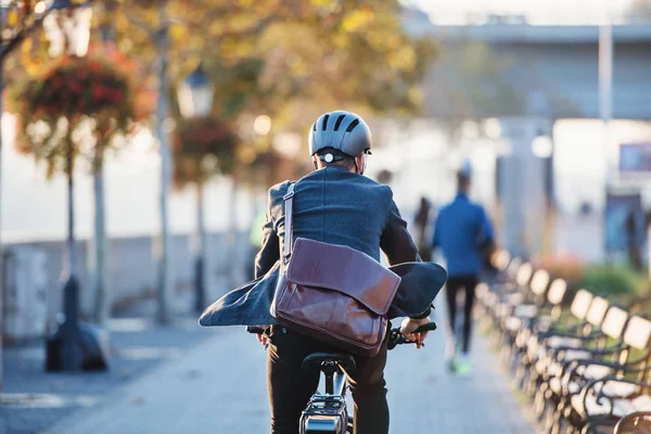 Una vista trasera del viajero de negocios con bicicleta eléctrica que viaja al trabajo en la ciudad . — Foto de Stock