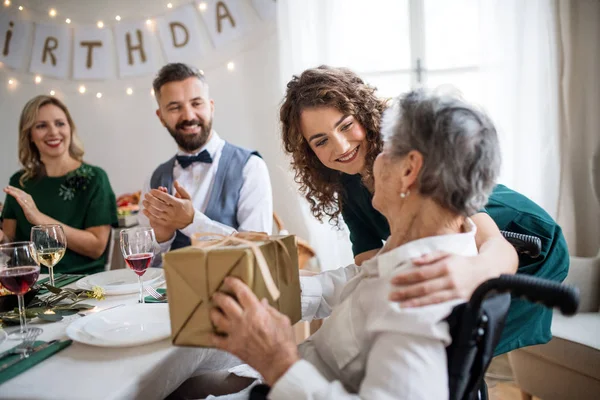 An elderly grandmother celebrating birthday with family and recieving a gift, party concept. — Stock Photo, Image