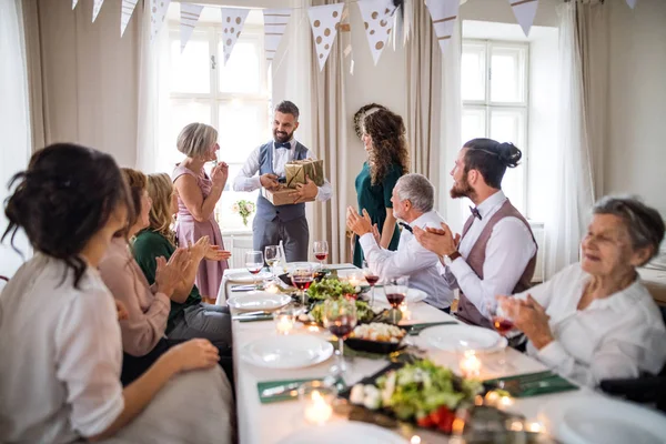 Una joven pareja dando un regalo a una madre en una fiesta de cumpleaños familiar . —  Fotos de Stock