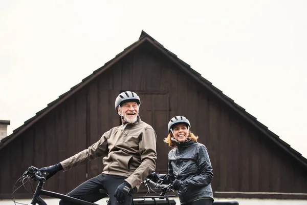 Active senior couple with electrobikes standing outdoors in front of a house. — Stock Photo, Image