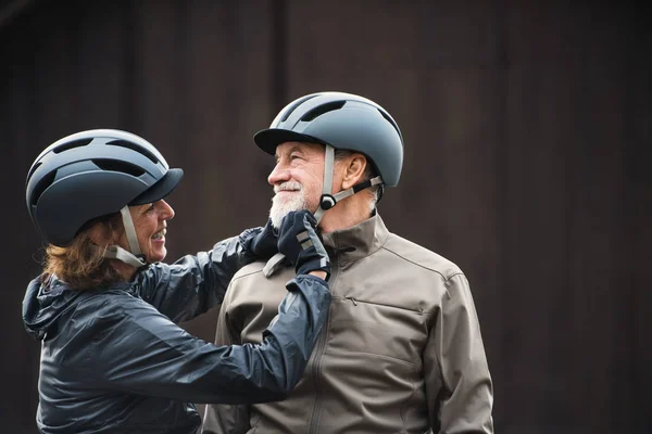 Активна старша пара з велосипедними шоломами, що стоять на відкритому повітрі, друкує темний фон . — стокове фото