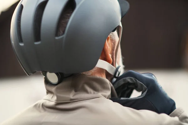 En bakre vy av aktiv senior man stående utomhus i stan, sätta på en cykelhjälm. — Stockfoto