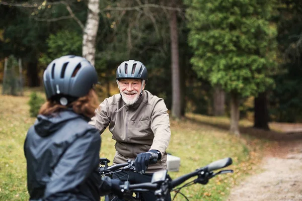 Ein älteres Ehepaar mit Fahrradhelm steht im Herbst draußen auf einer Straße im Park. — Stockfoto