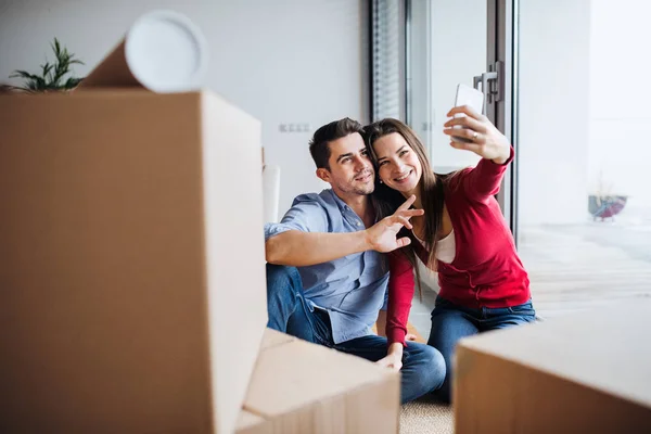 Mladý pár s kartony pohybující se v novém domově, přičemž selfie. — Stock fotografie