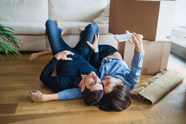A young couple with a smartphone moving in a new home, taking selfie. — Stock Photo, Image