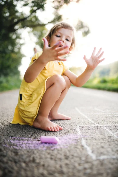 Piccola ragazza carina su una strada in campagna nella natura estiva soleggiata, disegno con gesso . — Foto Stock