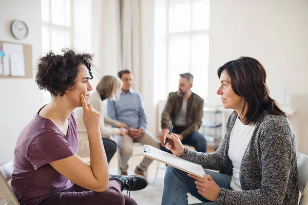 Senior counselor with clipboard talking to a woman during group therapy. — Stock Photo, Image