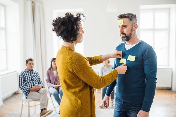 Counselor putting adhesive notes with the word sad on client during group therapy. — Stock Photo, Image