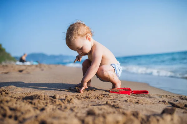 Una niña pequeña sentada en la playa en vacaciones de verano, jugando . —  Fotos de Stock