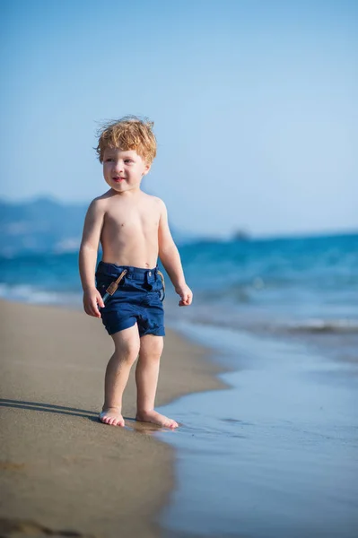 Seorang anak kecil dengan celana pendek berjalan di pantai pasir pada liburan musim panas . — Stok Foto