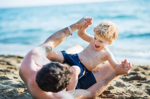Un padre con un hijo pequeño jugando en la playa de arena en las vacaciones de verano . — Foto de Stock