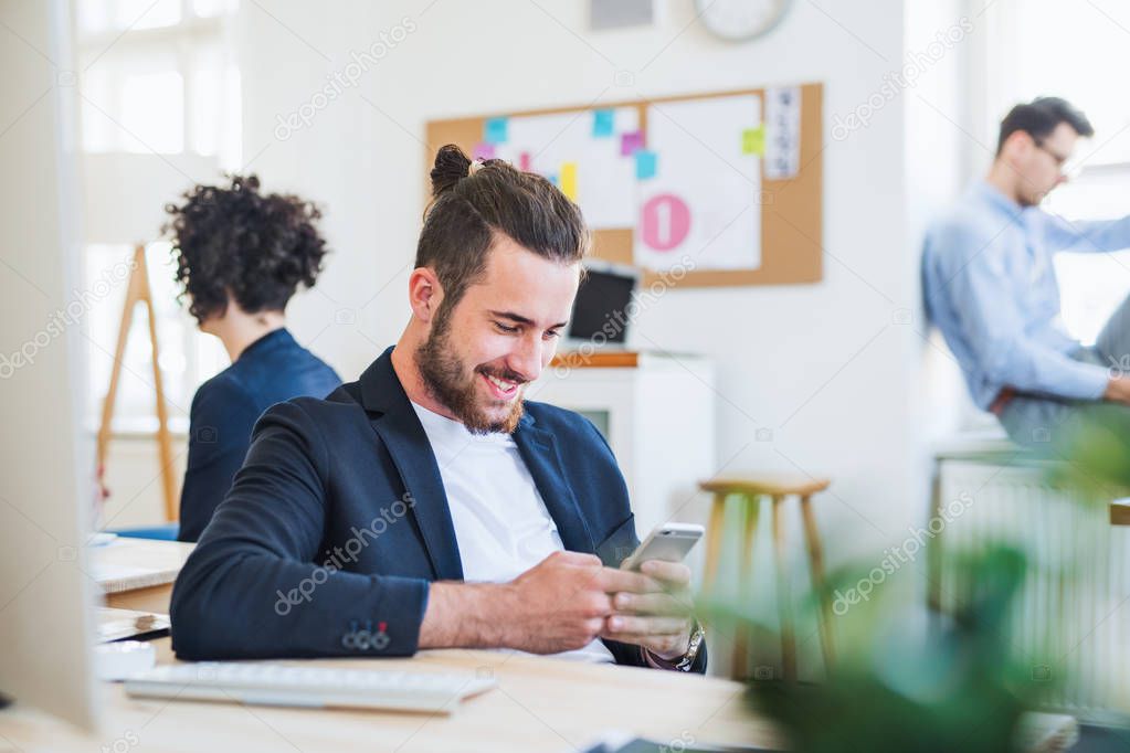 A portrait of young businessman with smartphone and colleagues in a modern office.