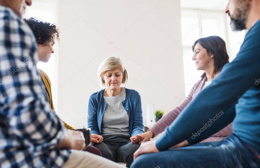 Men and women sitting in a circle and holding hands during group therapy.