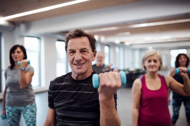 Neşeli yaşlılar dumbbells ile egzersiz yaparak spor salonunda Grup.