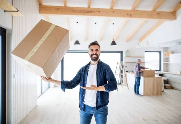 Un hombre maduro sosteniendo una caja grande en una mano al amueblar una casa nueva . — Foto de Stock