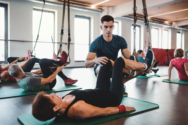 Neşeli yaşlılar Trx ile egzersiz yaparak genç bir eğitmen ile spor salonunda bir grup. — Stok fotoğraf