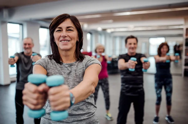 Groep van vrolijke senioren in sportschool doen oefening met halters. — Stockfoto