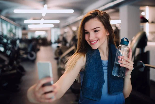 Portrét mladé dívky nebo ženy s smartphone v tělocvičně, přičemž selfie. — Stock fotografie