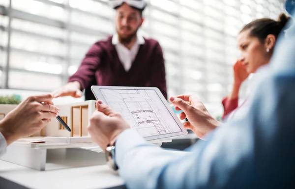 Skupina mladých architektů s tabletem a model dům, stojící v úřadu, mluví. — Stock fotografie