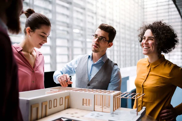 Group of young architects with model of a house standing in office, talking. — Stock Photo, Image