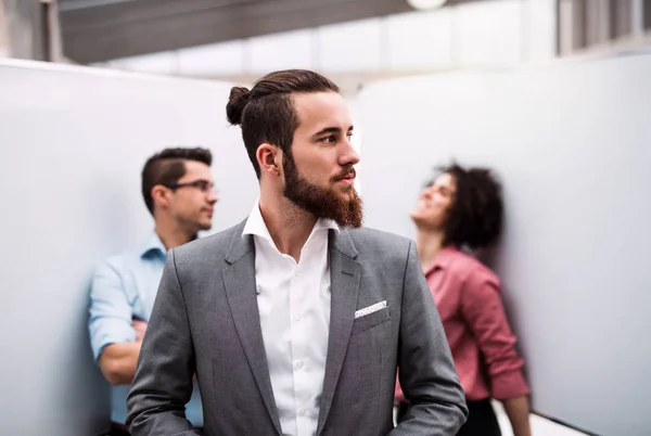 Un joven hombre de negocios en traje de pie en la oficina, colegas en el fondo . — Foto de Stock