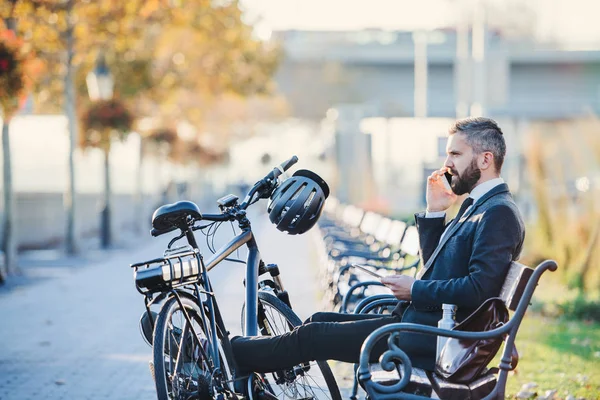Empresario viajero con bicicleta sentado en el banco de la ciudad, haciendo una llamada telefónica . — Foto de Stock