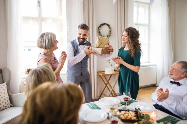 Una joven pareja dando un regalo a una madre en una fiesta de cumpleaños familiar . — Foto de Stock