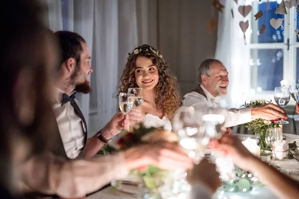Nevěsta a ženich na svatbě, cinkání brýle sedí u stolu. — Stock fotografie