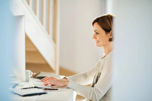 A happy young woman indoors, working in a home office. — Stock Photo, Image
