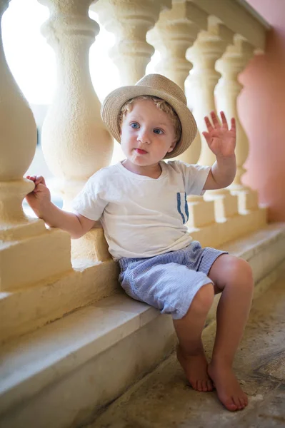 A portrait of small toddler boy sitting in front of concrete railing on summer holiday. — Stock Photo, Image