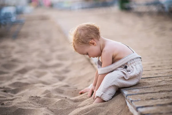 Ein kleines Mädchen, das im Sommerurlaub am Strand sitzt und spielt. — Stockfoto