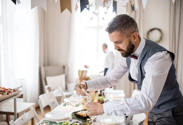 Homem maduro com arco e colete colocando uma mesa para uma festa interior . — Fotografia de Stock