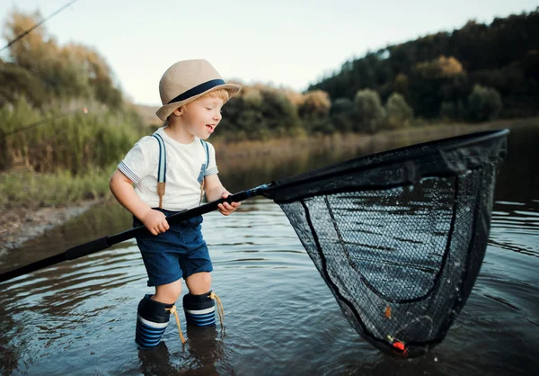 Malé batole chlapec stojí ve vodě a drží čisté jezero, rybaření. — Stock fotografie